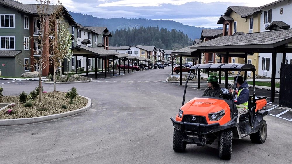 Maintenance team members driving an orange utility vehicle through a completed apartment community with covered parking.