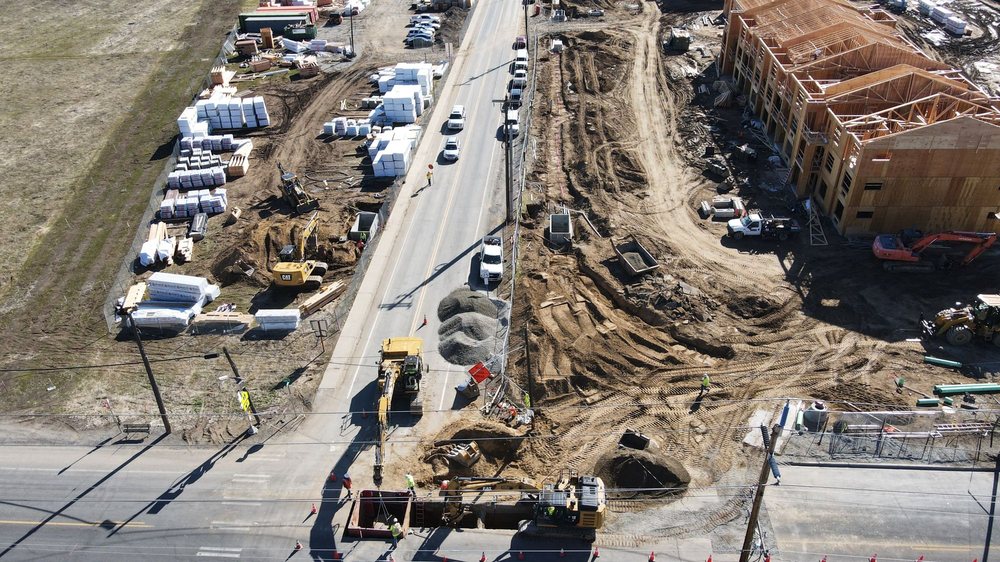 Aerial view of roadwork and active construction beside a multi-story wood-framed apartment building.