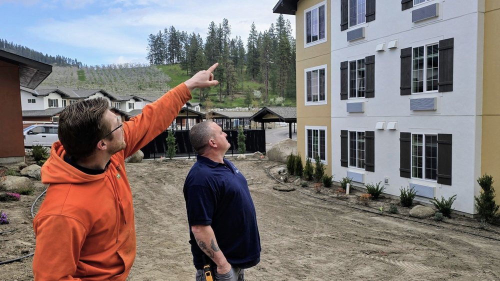 Two team members inspecting the exterior of a completed apartment building and pointing toward an upper floor.