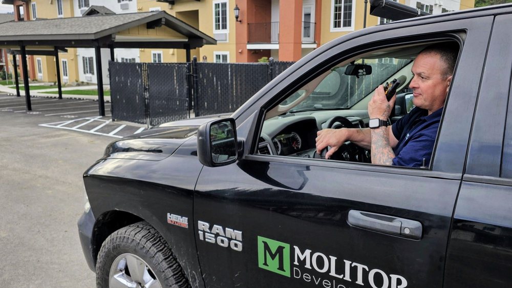 Construction manager using a handheld radio from a Molitor Development truck at a completed apartment community.