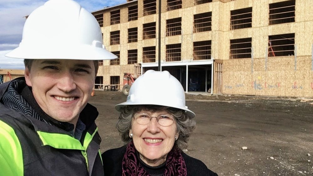 Construction manager and resident wearing hard hats during a visit to a multi-story building under construction.