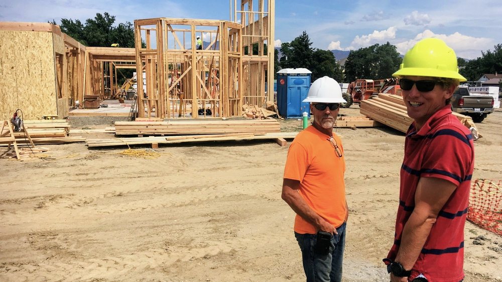 Two members of a construction team wearing hard hats at a wood-framed building site.