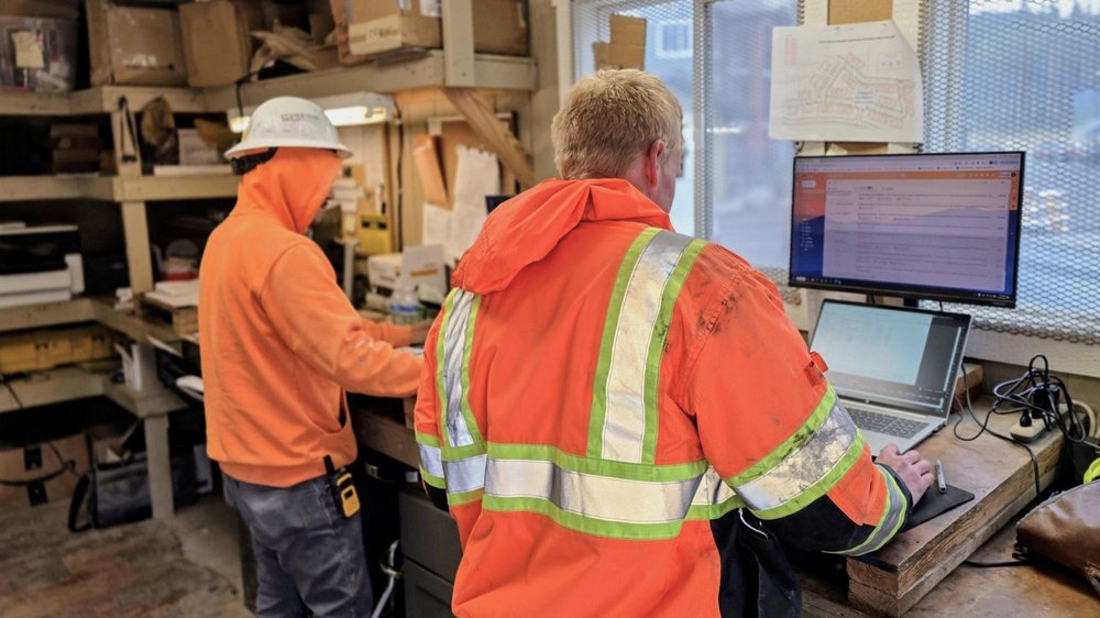 Construction team members reviewing project information on a computer inside a jobsite office.