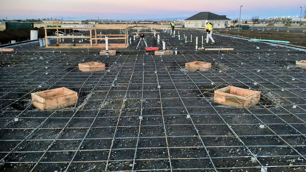 Foundation rebar grid, plumbing lines, and wood forms prepared before a concrete slab pour.