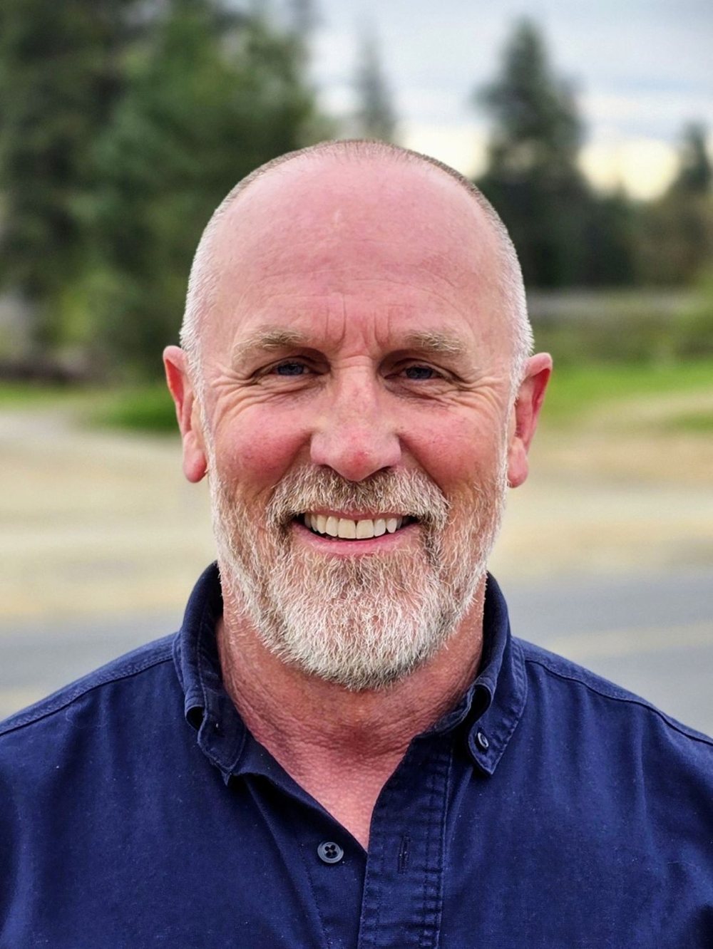Headshot of Greg smiling outdoors in a navy button-down shirt.