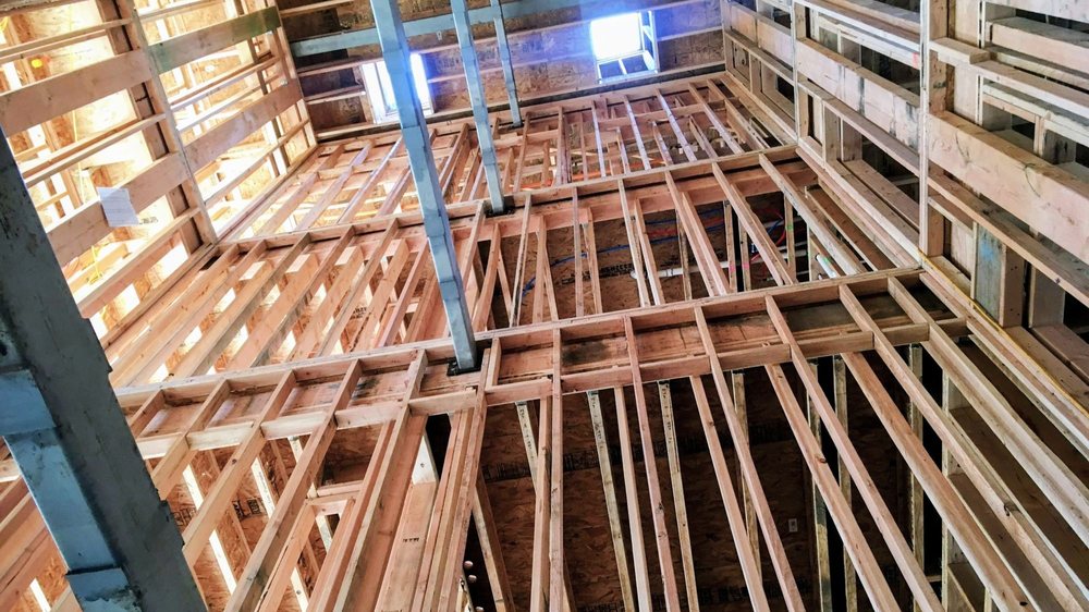 Interior view looking upward through the multi-story wood framing of a building under construction.