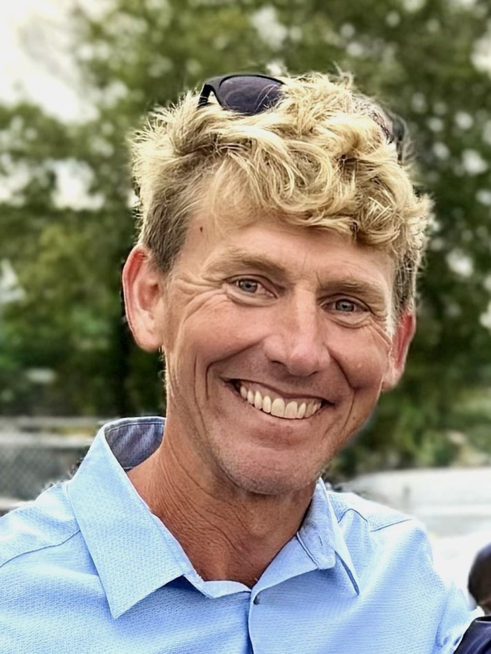 Headshot of Mitch smiling outdoors in a light blue button-down shirt.