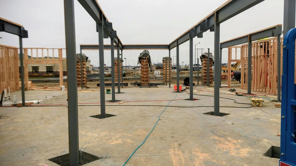 Steel beams and columns installed on a concrete slab alongside wood framing at an active construction site.