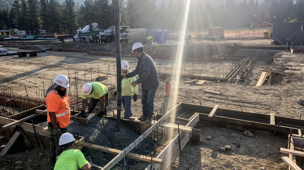 Construction workers pouring concrete into foundation forms at an active jobsite in the morning sunlight.