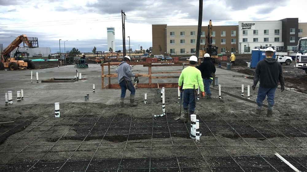 Construction workers preparing a concrete slab with plumbing lines and reinforcement in place at a commercial jobsite.