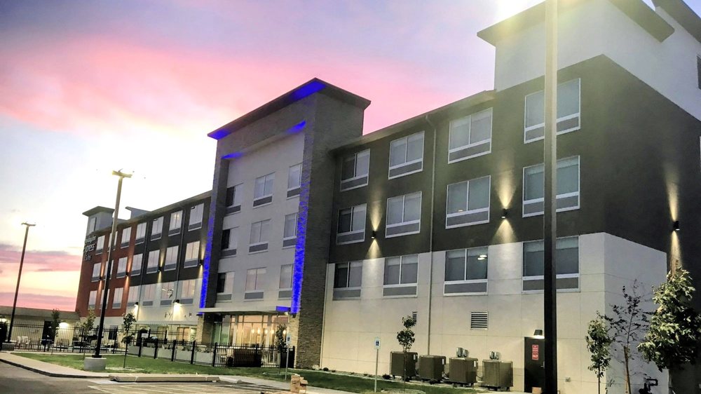 Modern hotel exterior illuminated at sunset with landscaped grounds and a colorful evening sky.