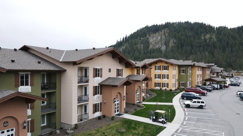 Colorful apartment buildings with balconies, landscaped walkways, and forested mountains in the background.