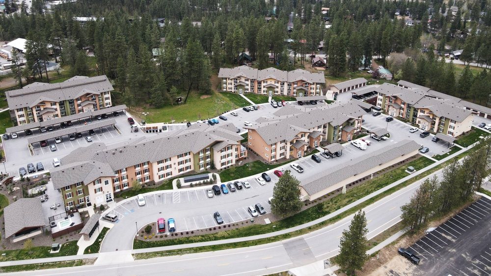 Wide aerial view of a large apartment community surrounded by pine trees and mountain terrain.