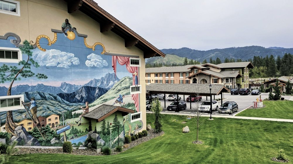 Large mountain-themed mural overlooking a landscaped apartment courtyard with covered parking.