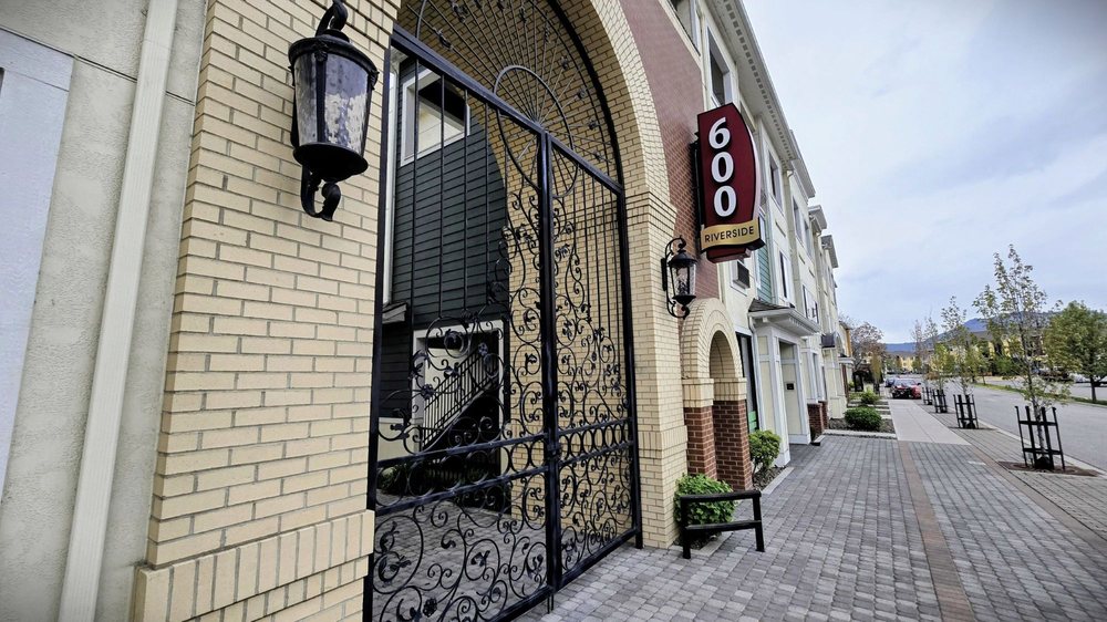 Decorative gated entrance and 600 Riverside sign along a brick-lined city sidewalk.
