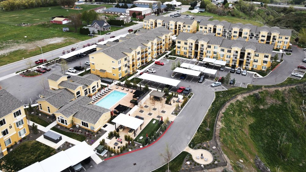 Aerial view of a yellow apartment community with a swimming pool, courtyard seating, and covered parking.
